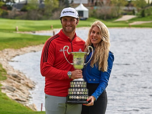 Jon Rahm and his wife Kelley Cahill celebrate together at a golf tournament with the championship trophy.